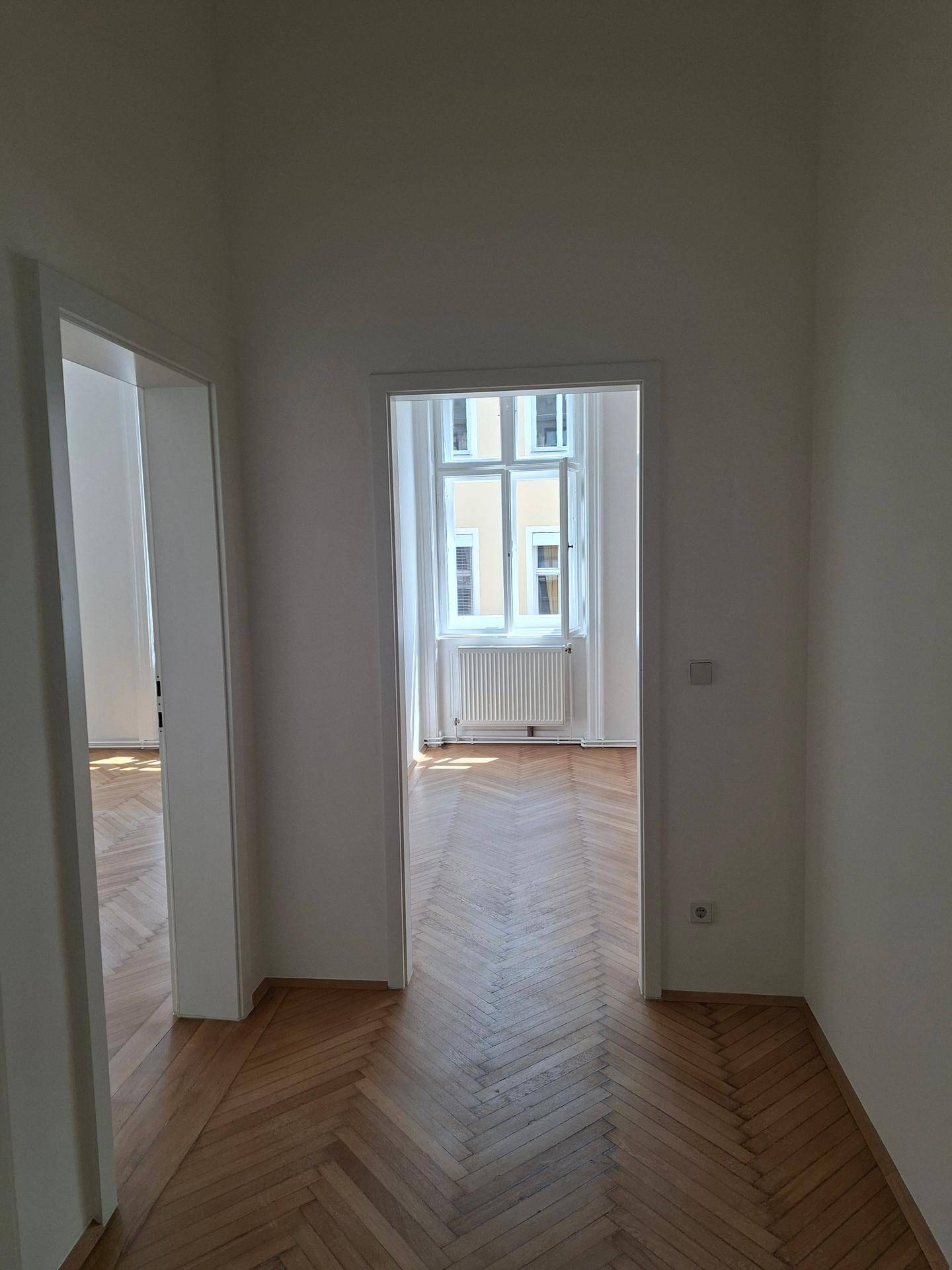 Flur mit Fischgrätparkettboden, der den Blick in ein weiteres helles Zimmer freigibt.