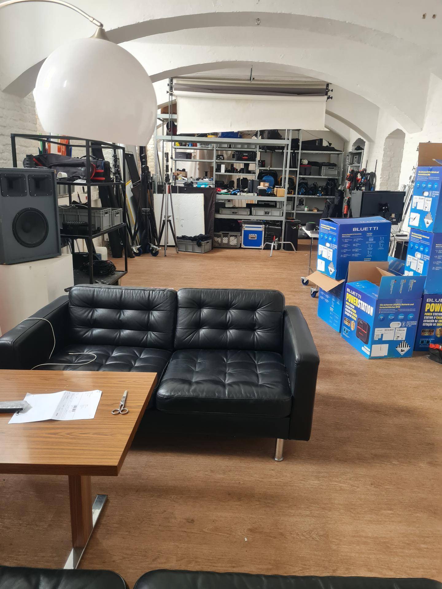 Großer offener Raum mit schwarzem Ledersofa, Holztisch und Regalen im Hintergrund.