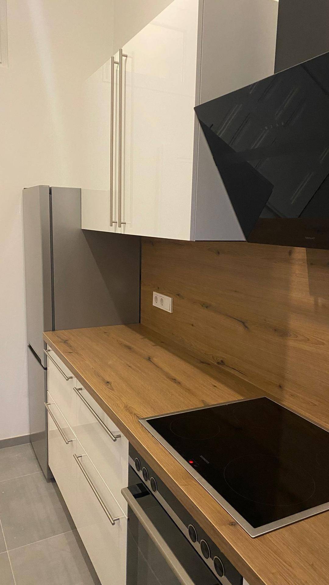 Moderne Einbauküche mit weißen Fronten, Holzarbeitsplatte und integriertem Kühlschrank.
