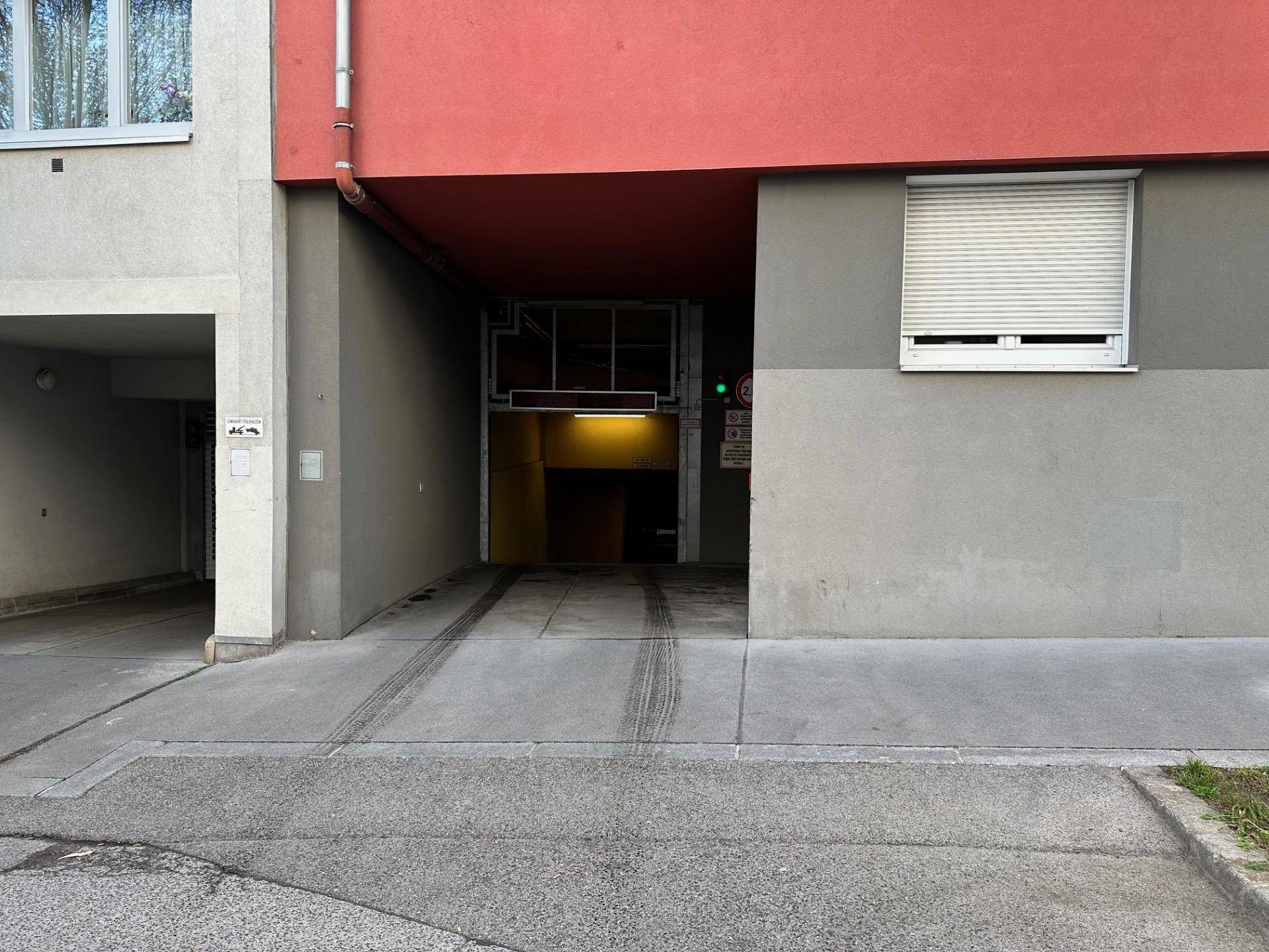 Einfahrt zur Tiefgarage mit roter Fassade und Rollladen am Fenster.