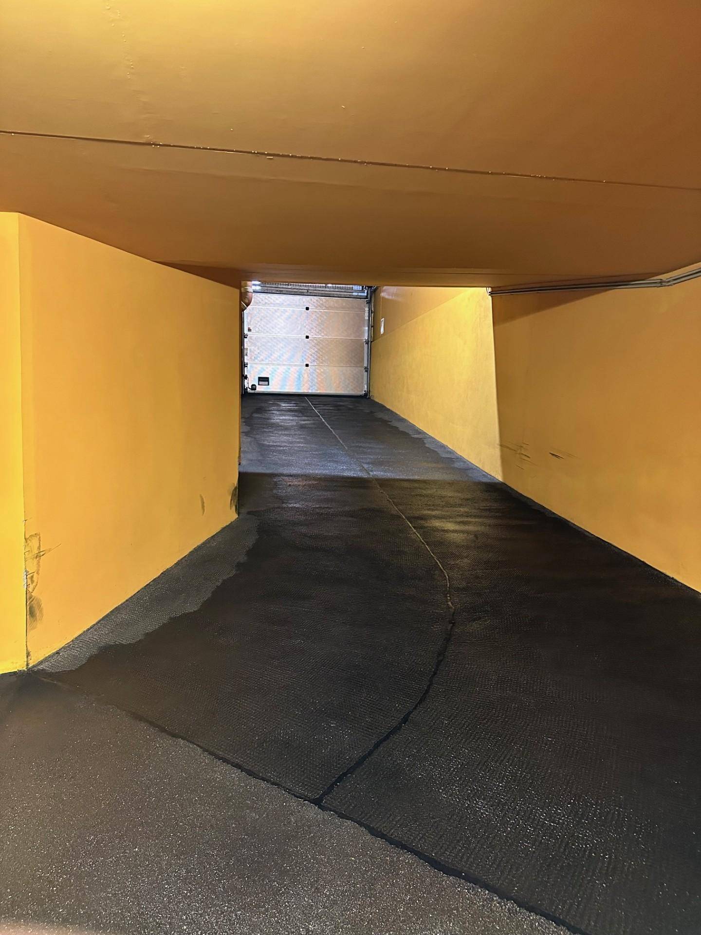 Zufahrtsrampe in einer Tiefgarage mit leuchtend gelben Wänden und dunklem Boden.