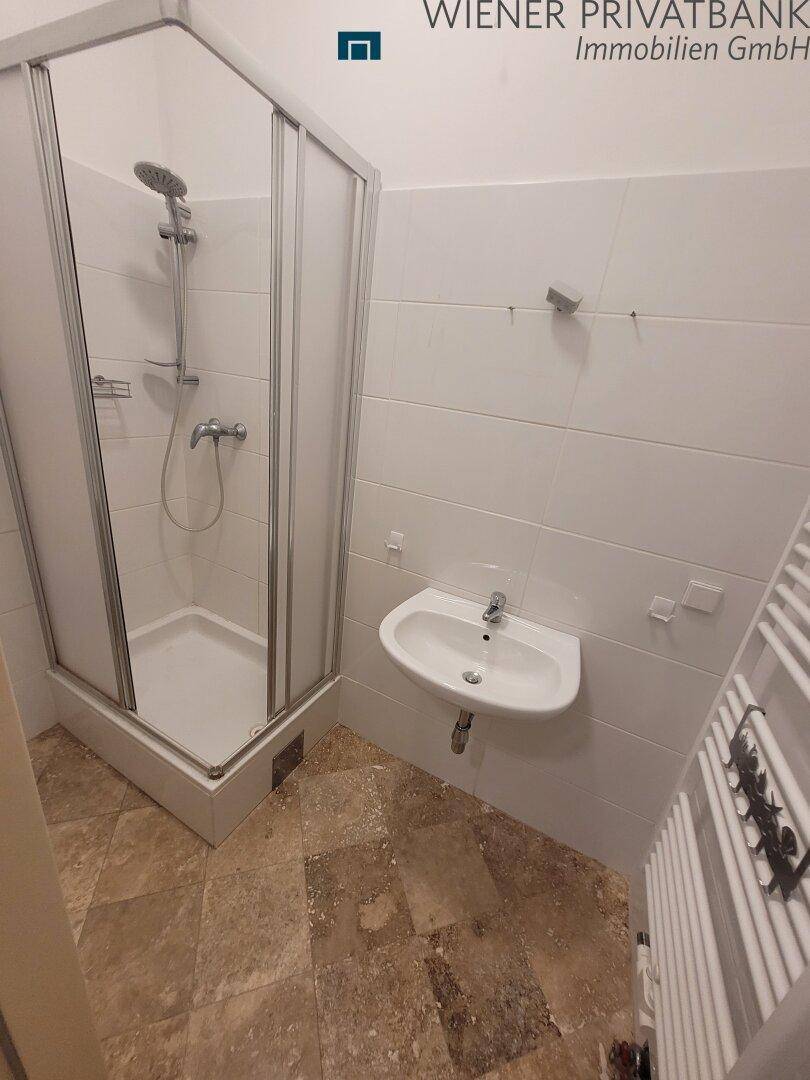 Kleines Badezimmer mit Duschkabine, Waschbecken und Fliesenboden.