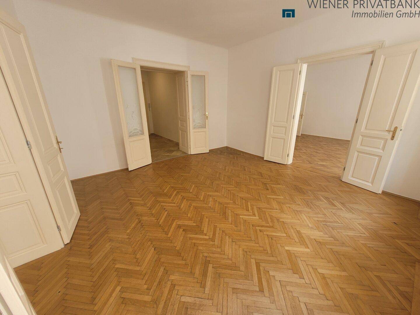Geräumiges Zimmer mit Fischgrätparkett und mehreren Türen, ideal für Wohnzwecke.