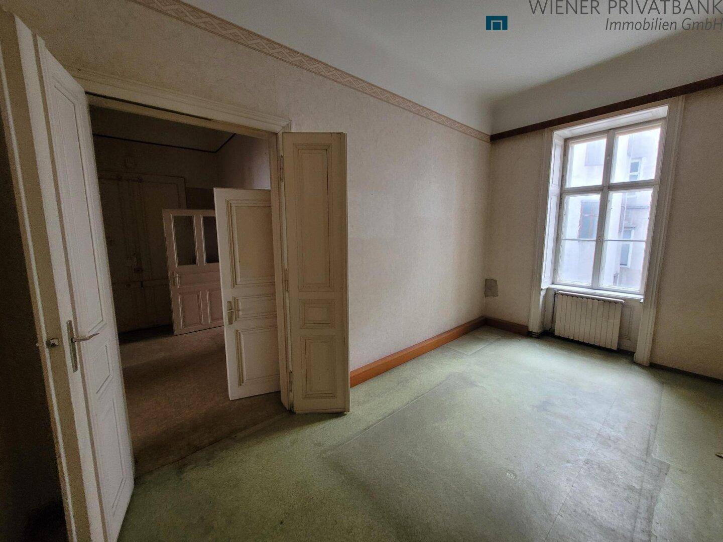 Innenraum mit altem Teppichboden, Fenster und offenen Türen, der eine Modernisierung erfordert.