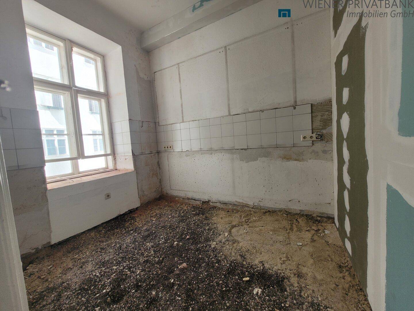 Küche in Renovierung mit alten Wandfliesen und einem Fenster, bereit für eine Neugestaltung.