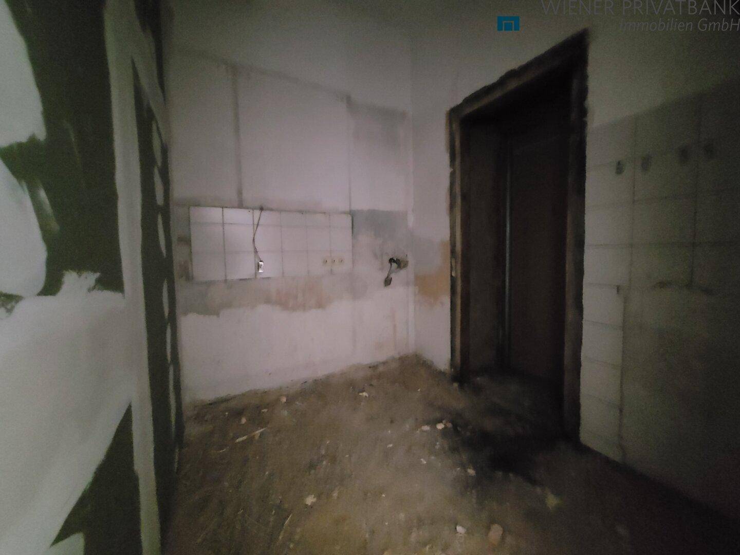 Dunkler Raum in Renovierungsphase mit sichtbaren Wandfliesen und unfertigem Boden.