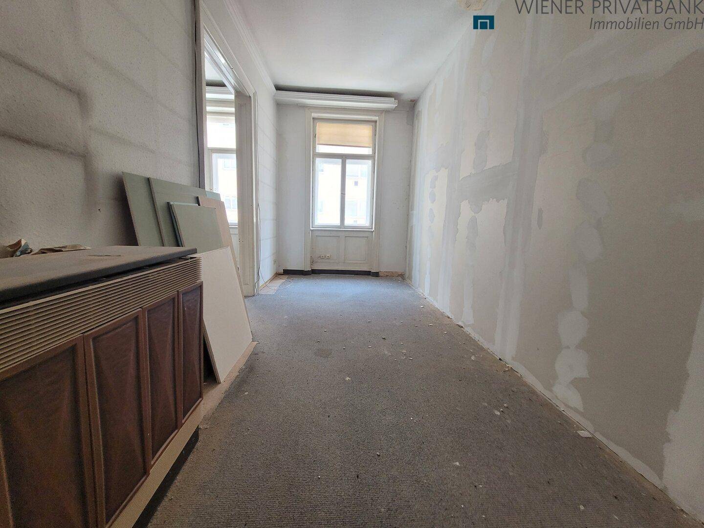 Langer Innenraum in Renovierungsphase mit Fenster am Ende und unfertigen Wänden.