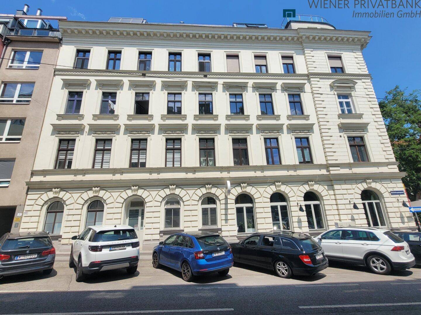 Klassisches Mehrfamilienhaus mit eleganter Fassade und parkenden Autos davor.