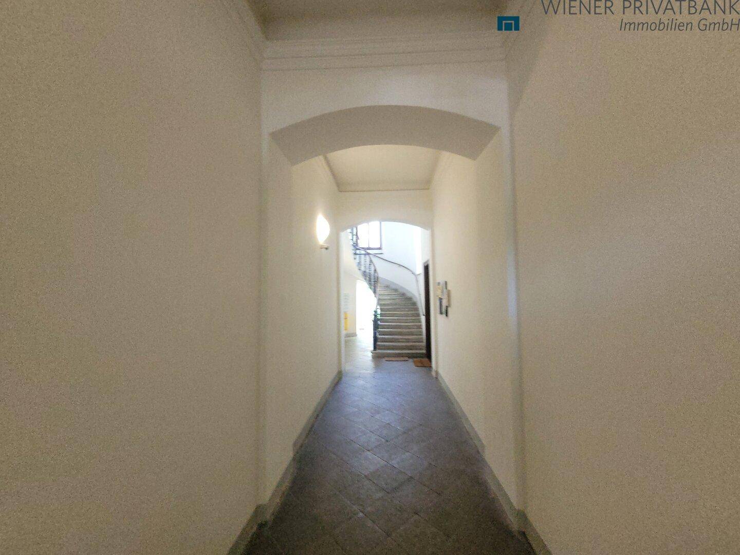 Langer Flur mit Fliesenboden und einem Bogen, der zum Treppenhaus führt.