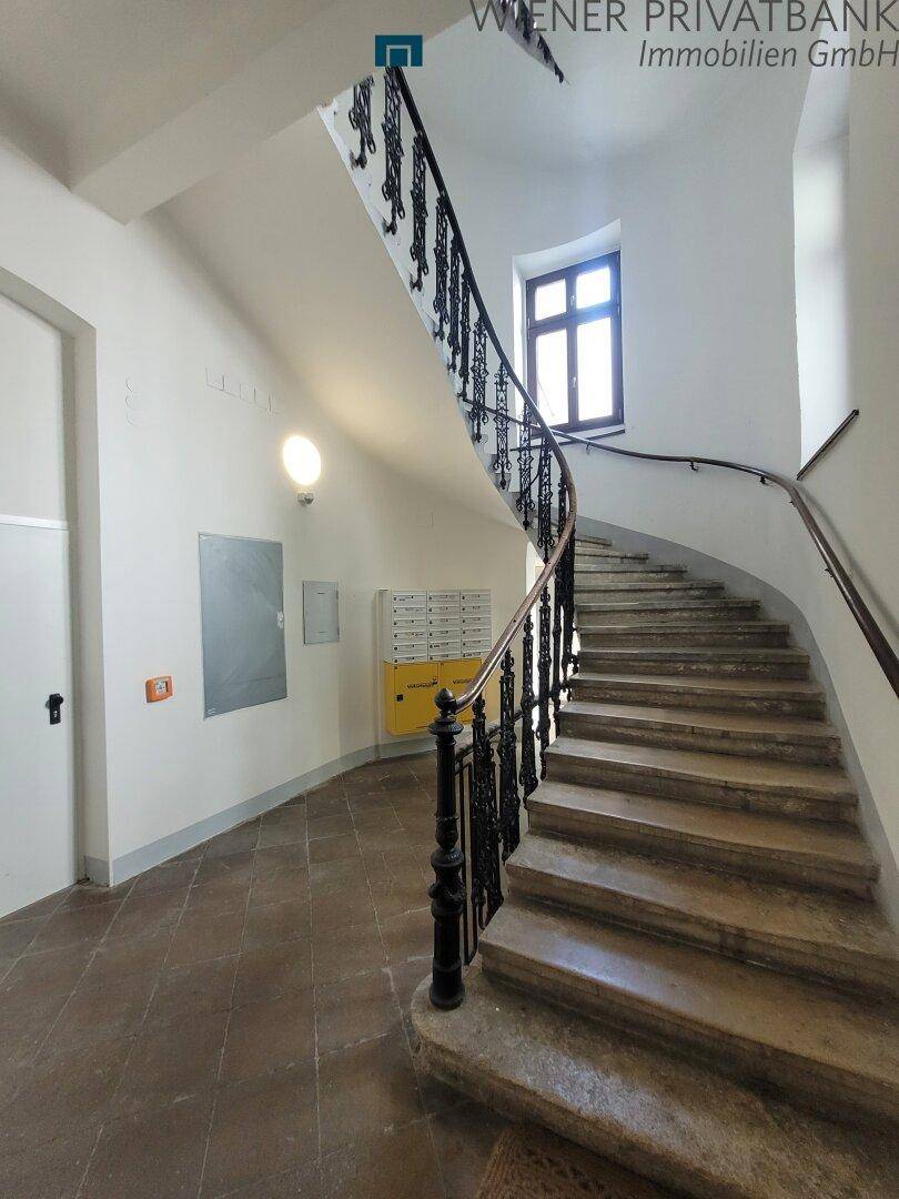 Eingangsbereich mit geschwungener Steintreppe, schmiedeeisernem Geländer und Briefkästen.