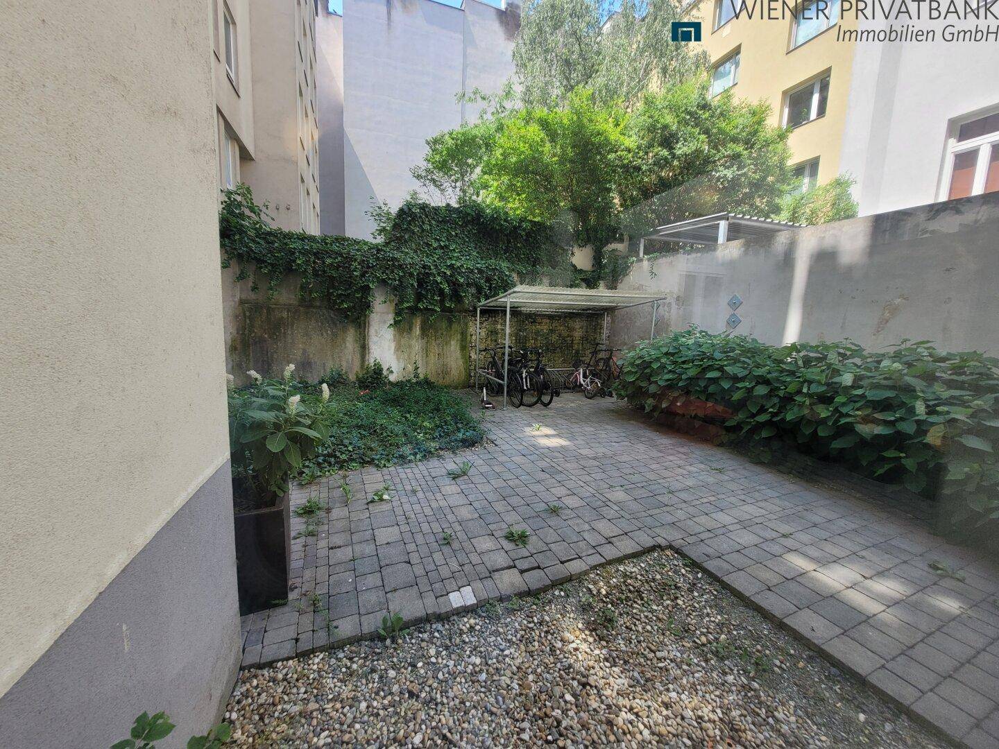 Hinterhof mit gepflastertem Bereich, Fahrradunterstand und viel Grünbewuchs an den Wänden.