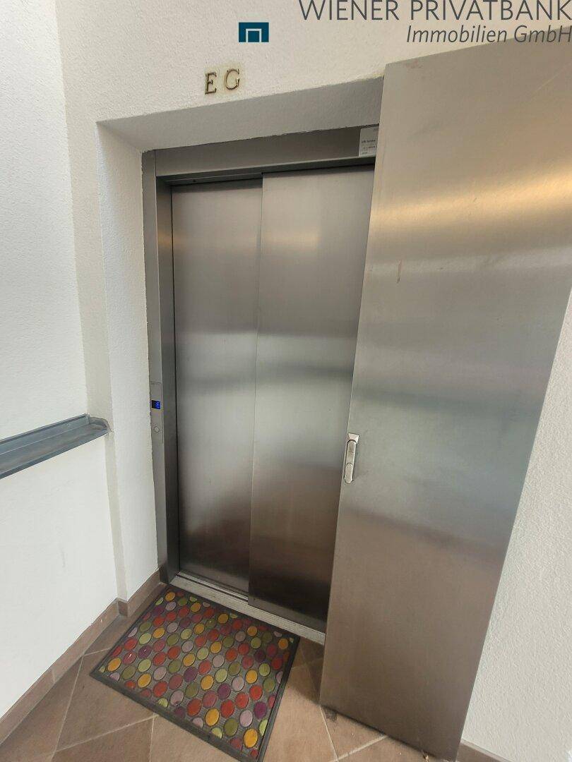 Moderner Aufzug aus Edelstahl im Erdgeschoss eines Wohngebäudes.
