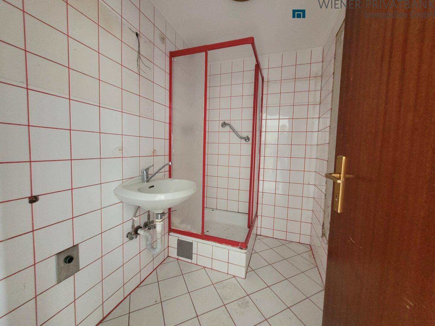 Badezimmer mit weißen Fliesen, roten Fugen und einer einfachen Duschkabine.