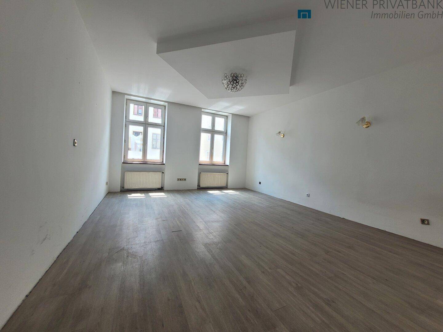 Geräumiges, unmöbliertes Zimmer mit hellem Laminatboden und zwei großen Fenstern.