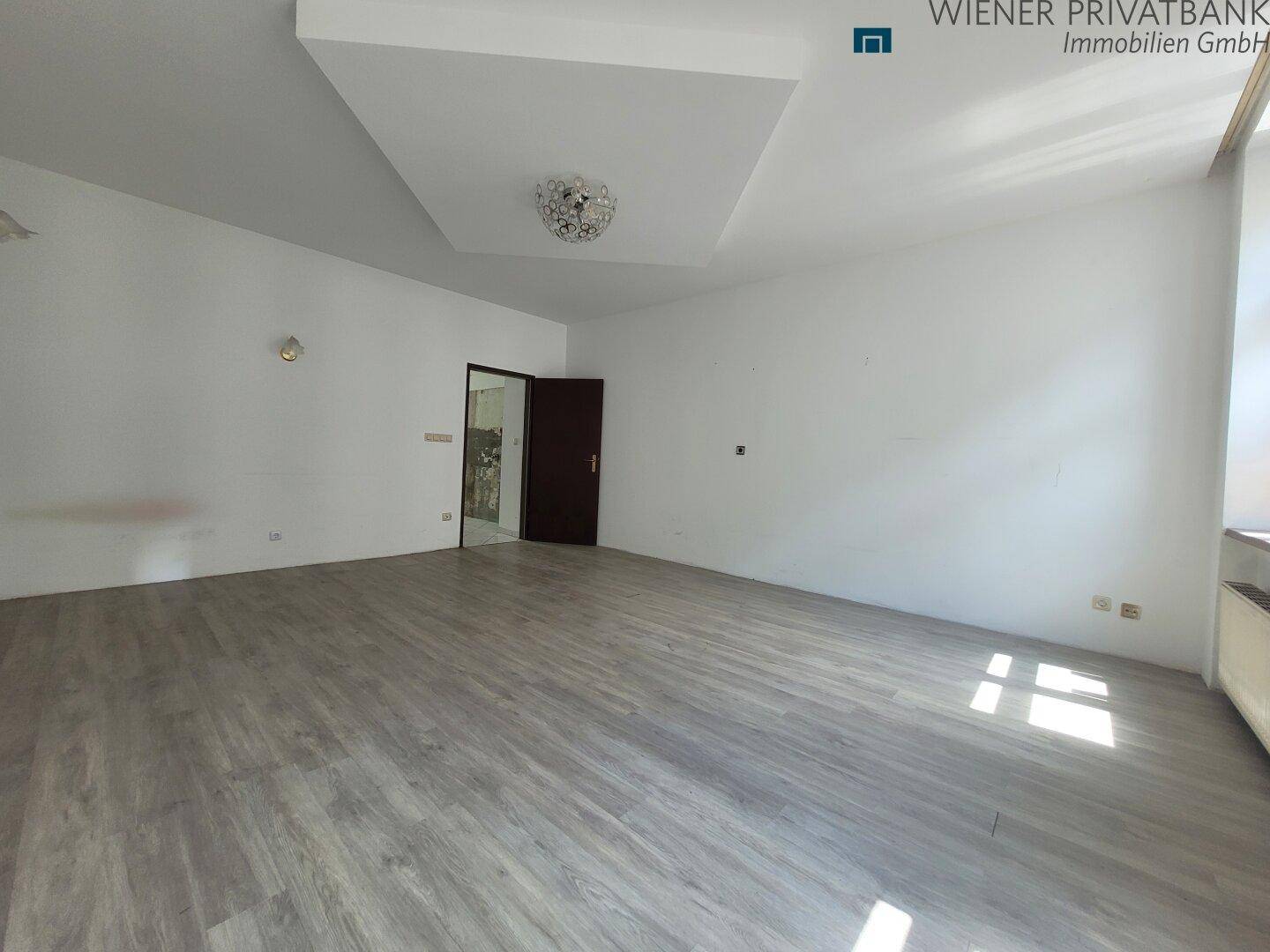 Helles, unmöbliertes Zimmer mit Laminatboden und Zugang zu einem weiteren Raum.