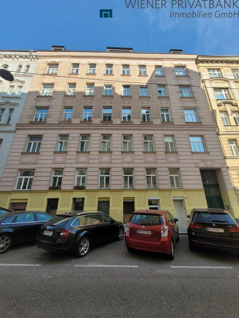 Historisches Mehrfamilienhaus mit klassischer Fassade und parkenden Autos davor.