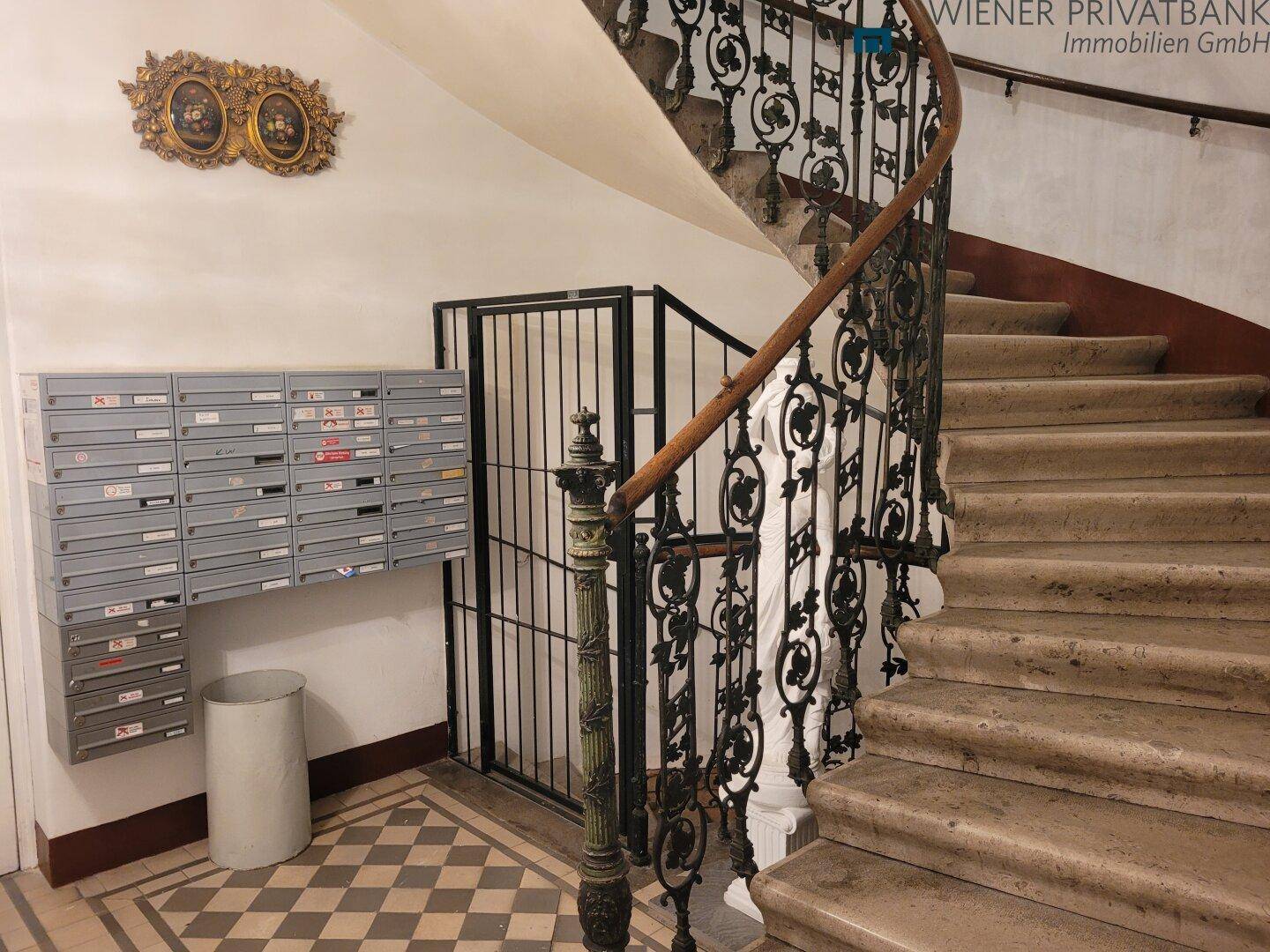 Historisches Treppenhaus mit schmiedeeisernem Geländer, Steinstufen und Briefkästen.