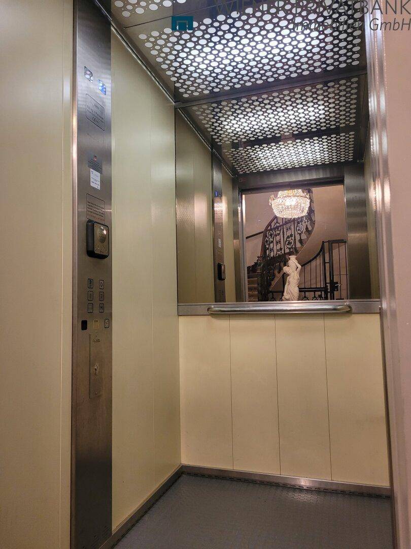 Moderner Aufzug mit Edelstahlelementen und einem Spiegel, der das Treppenhaus reflektiert.