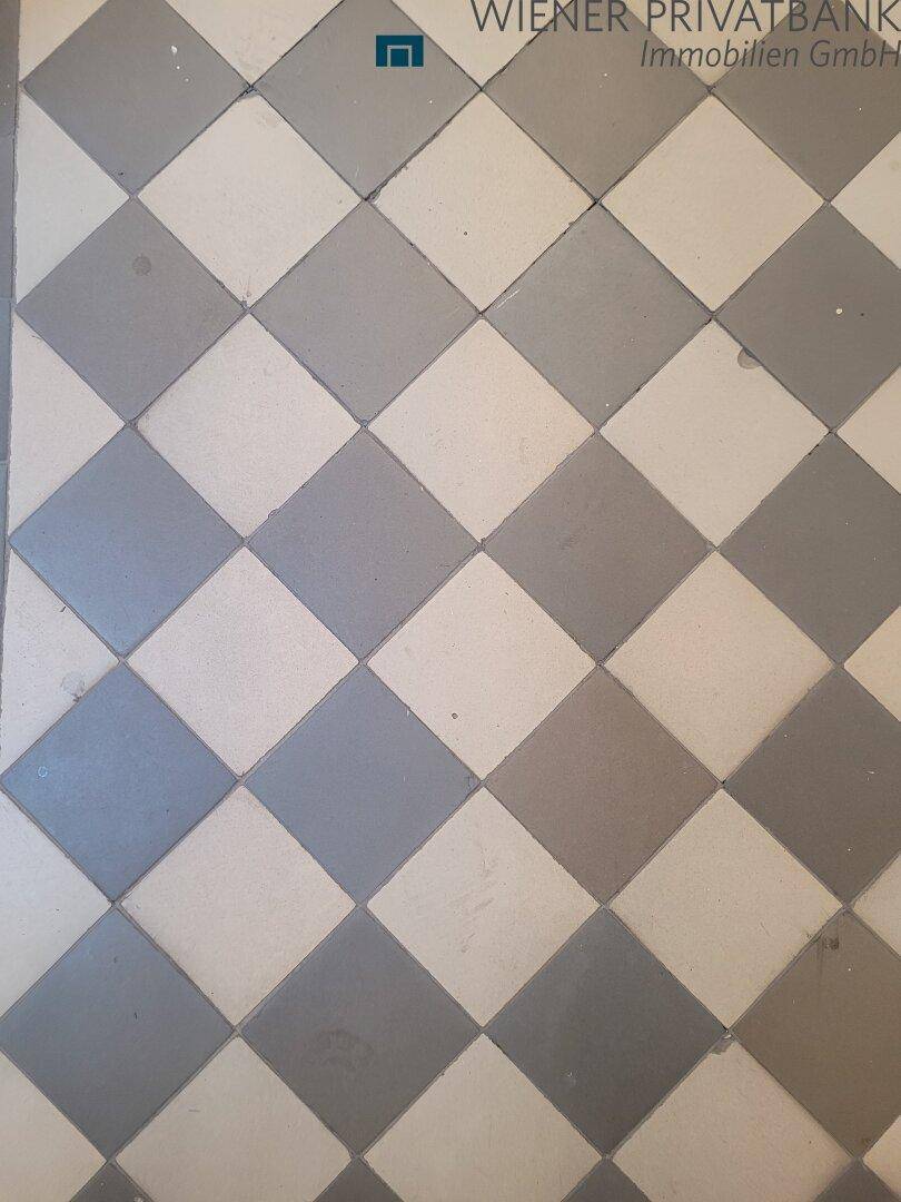 Nahaufnahme eines historischen Fliesenbodens mit einem Schachbrettmuster in Grau und Weiß.