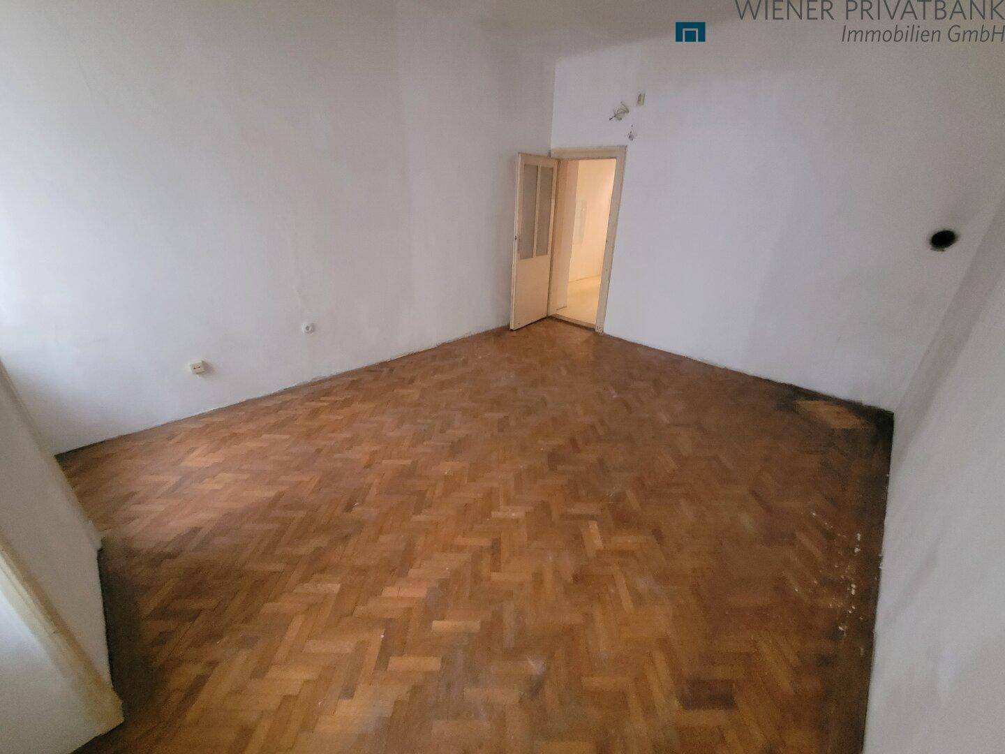 Leeres Zimmer mit Fischgrätparkett und einer Tür, die zu einem weiteren Raum führt.