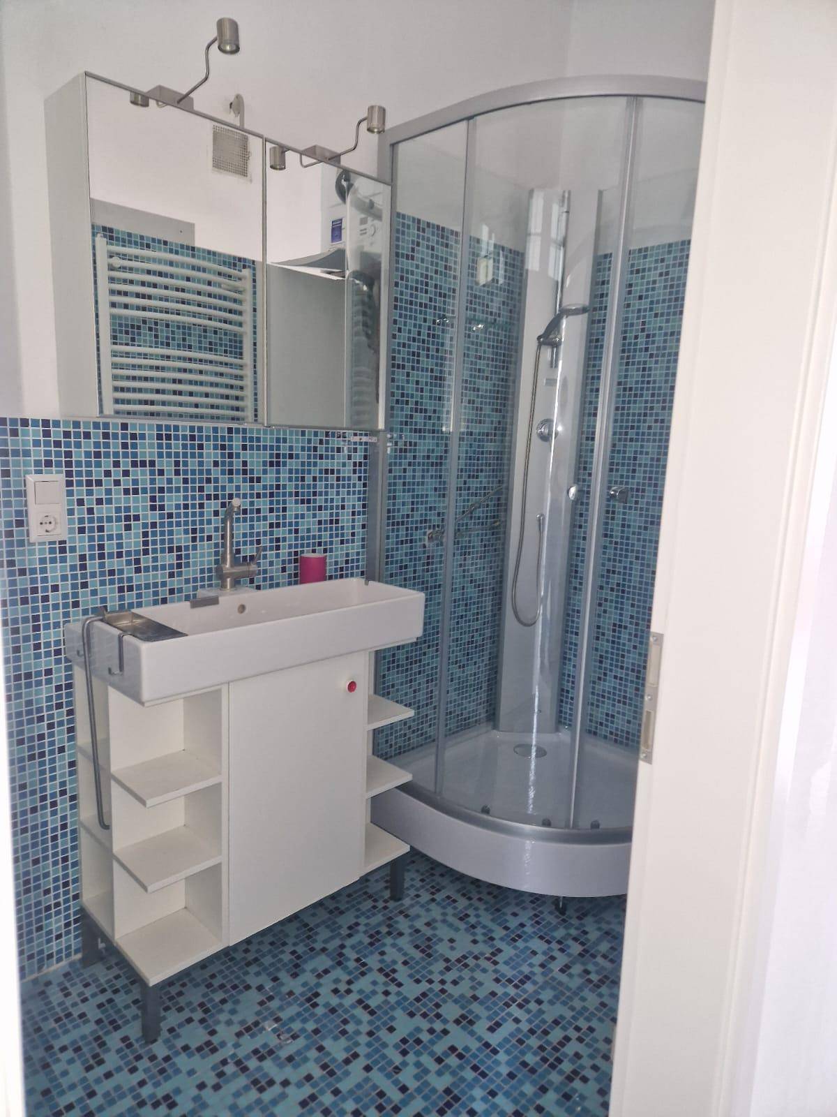 Modernes Badezimmer mit Duschkabine, Waschbecken und Spiegelschrank, komplett gefliest.