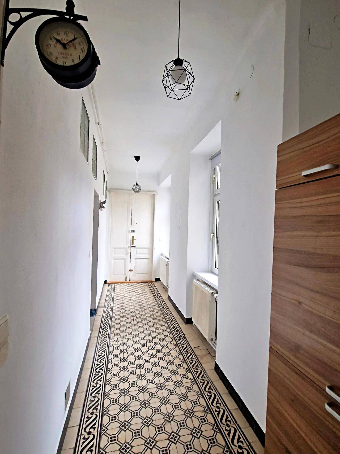 Langer Flur mit dekorativem Fliesenboden und Holzschrank, führt zu weiteren Räumen.