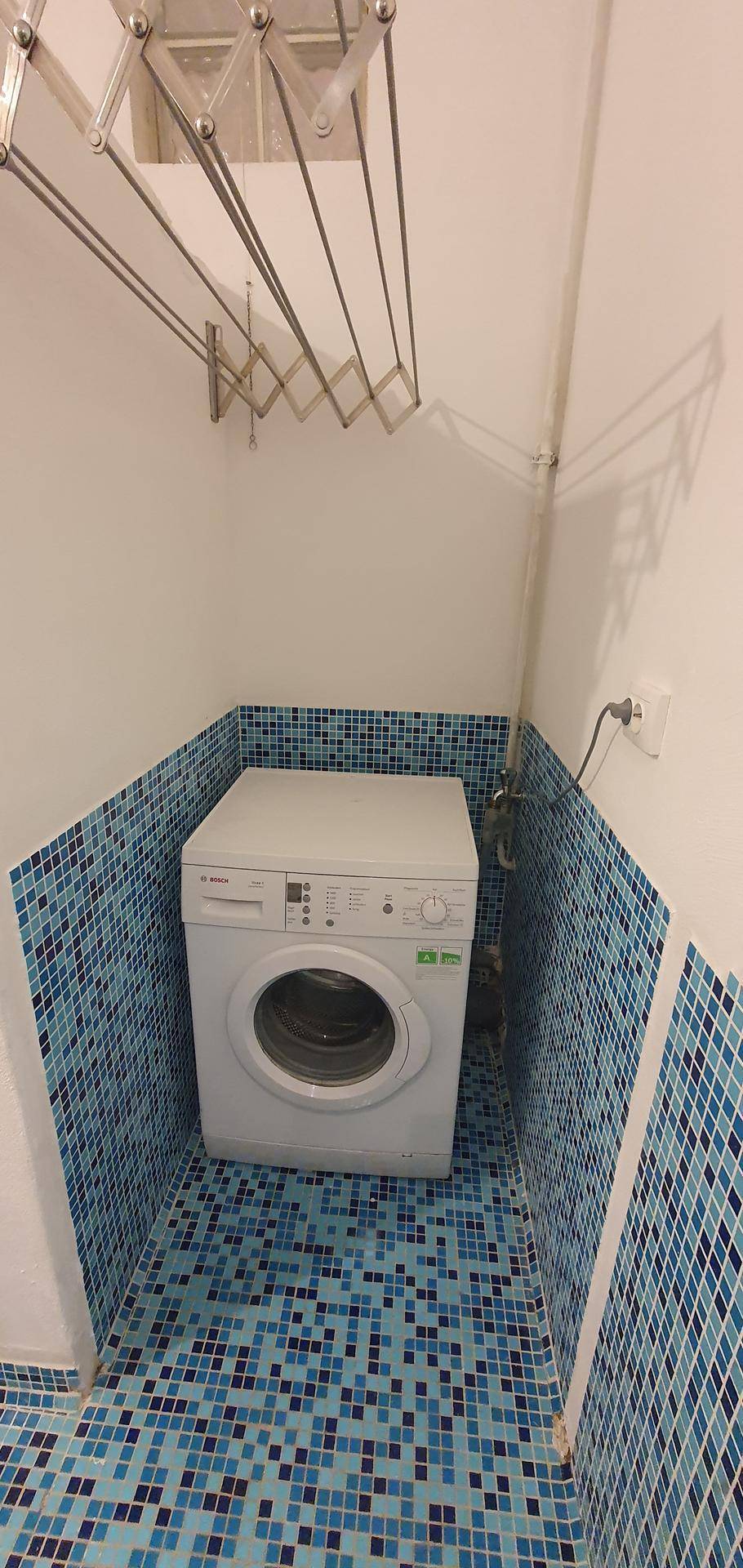 Praktischer Waschraum mit Waschmaschine und blauen Mosaikfliesen, ideal für den Haushalt.