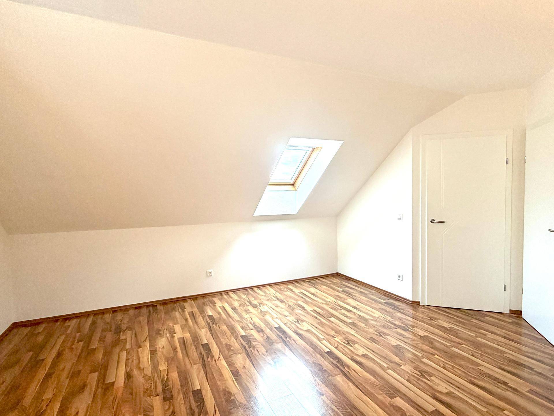 Leeres Schlafzimmer im Dachgeschoss mit Holzboden und Dachfenster.