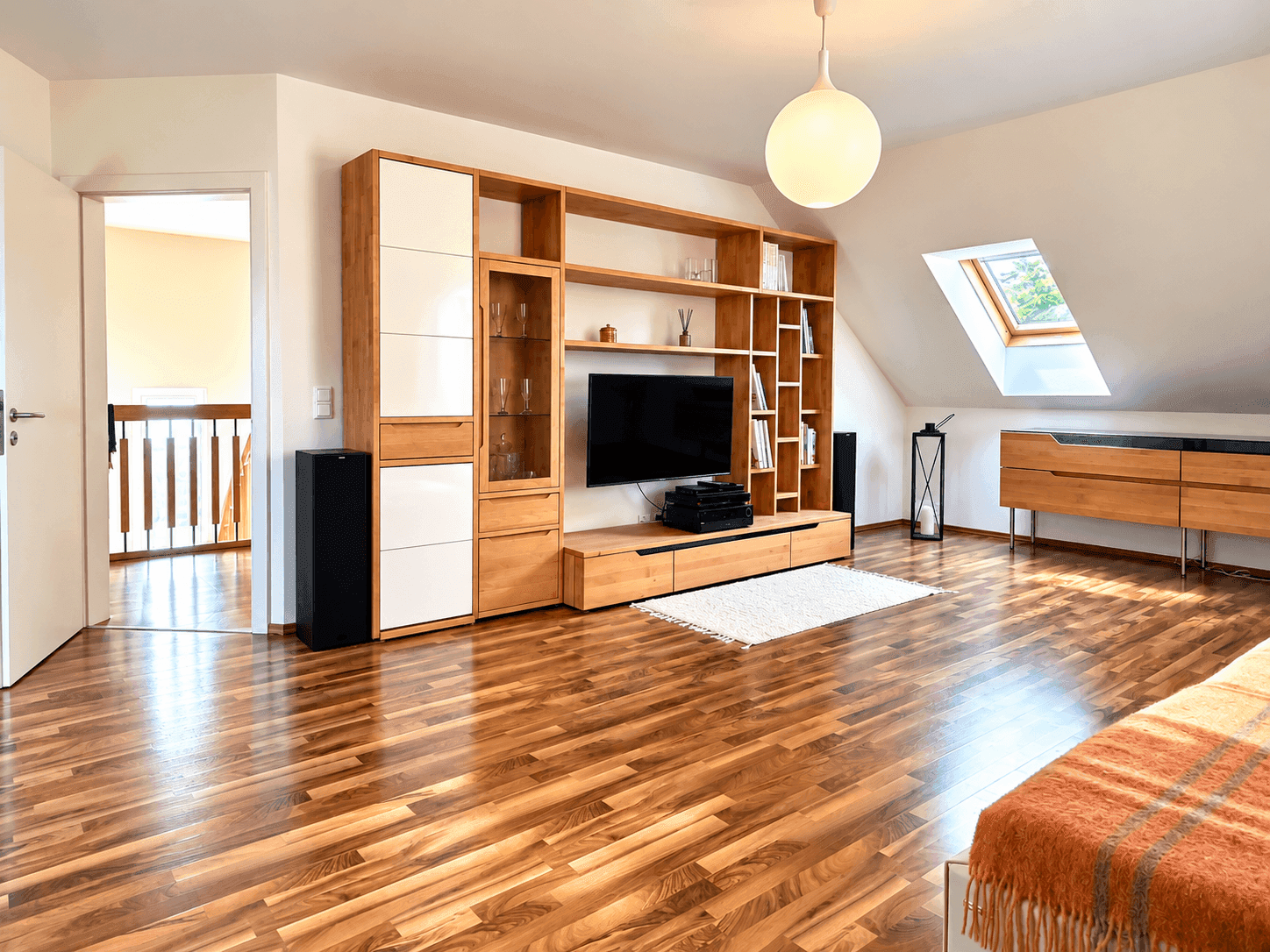 Gemütlicher Wohnbereich im Dachgeschoss mit Holzboden, Medieneinheit und Dachfenster.