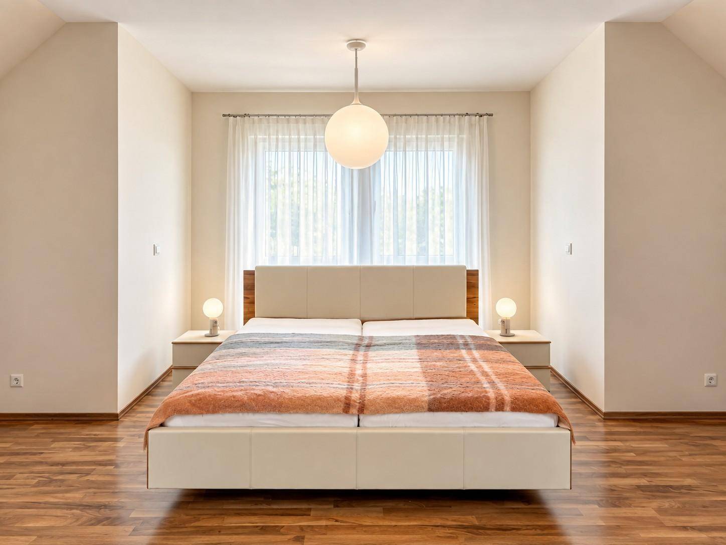 Helles Schlafzimmer mit Holzboden, Doppelbett und Dachschrägen im Obergeschoss.