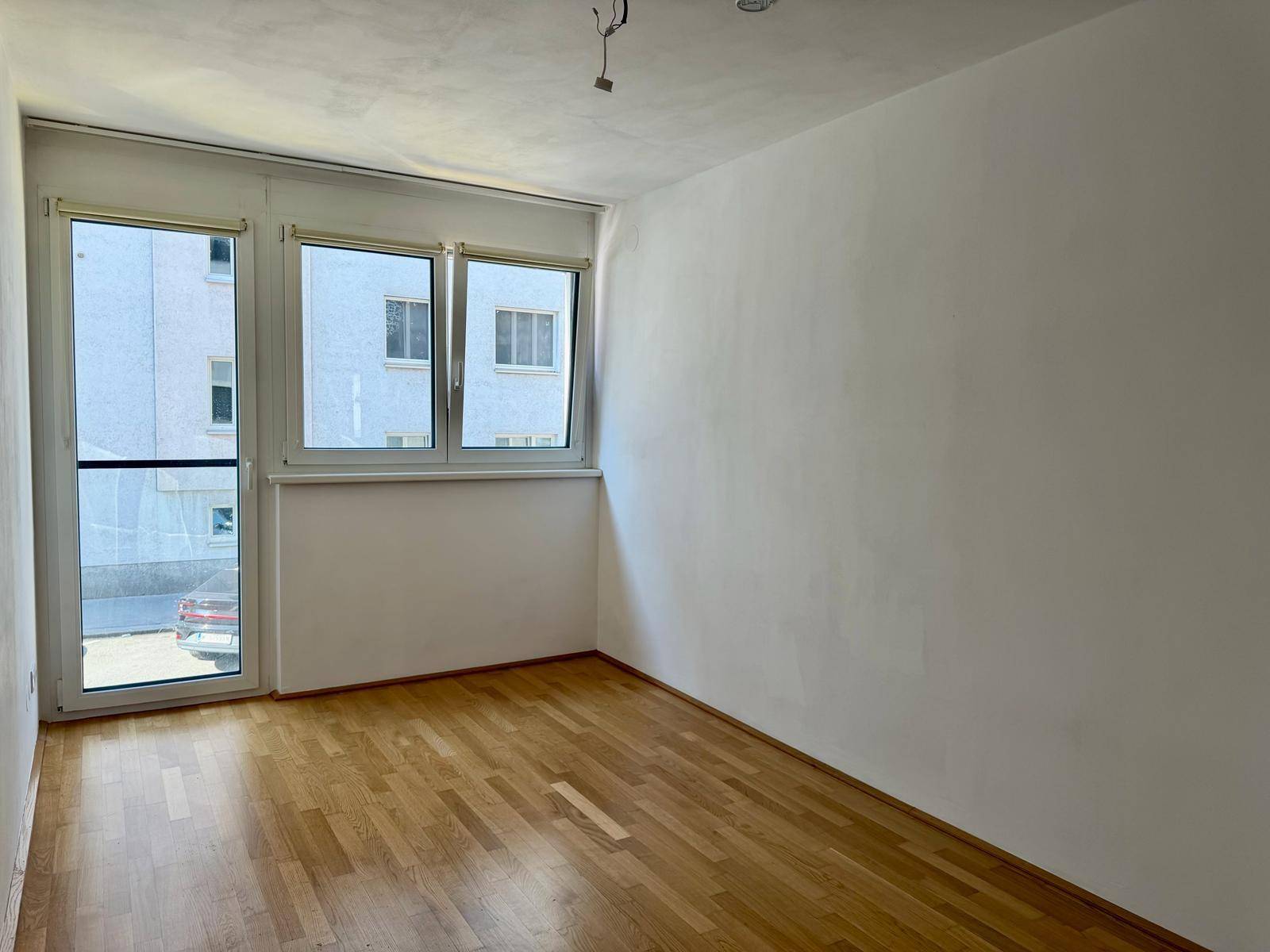 Leeres Zimmer mit Holzboden und großen Fenstern, bereit zur individuellen Gestaltung.