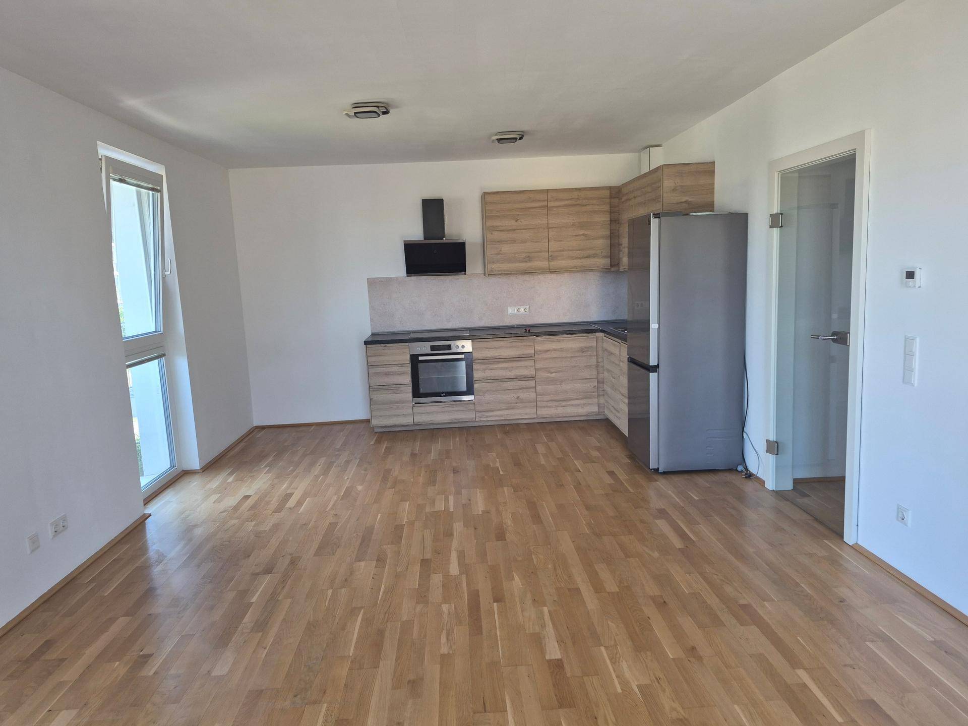 Offene Wohnküche mit modernen Holzschränken, integrierten Geräten und hellem Parkettboden.