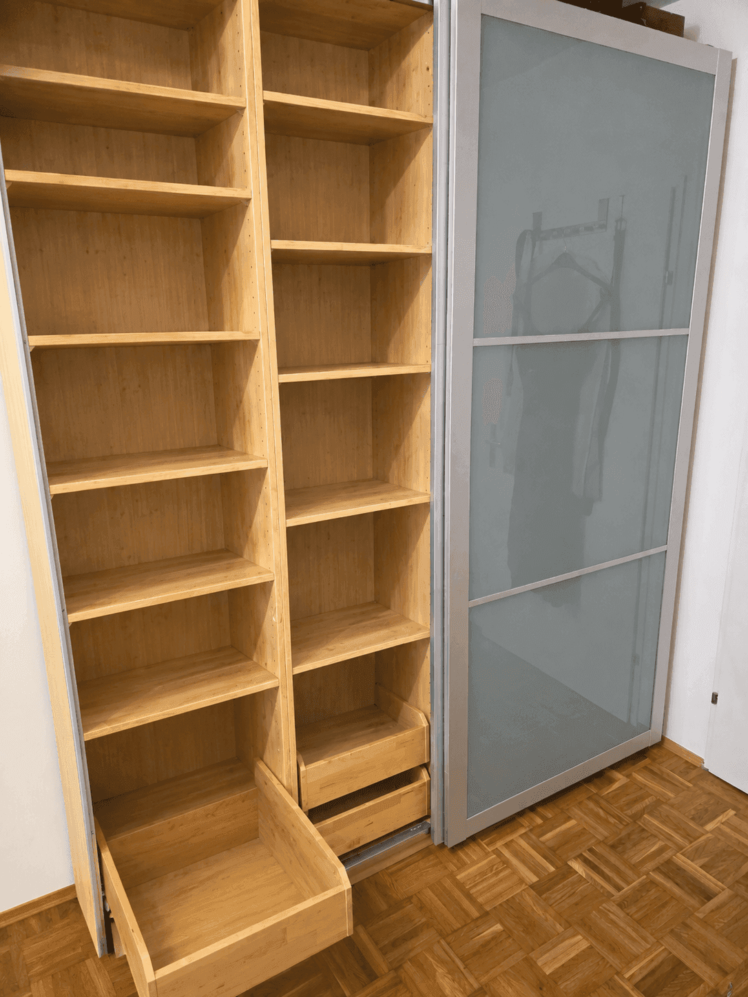 Maßgefertigter Kleiderschrank mit Holzregalen und Schiebetüren aus Milchglas auf Parkettboden.