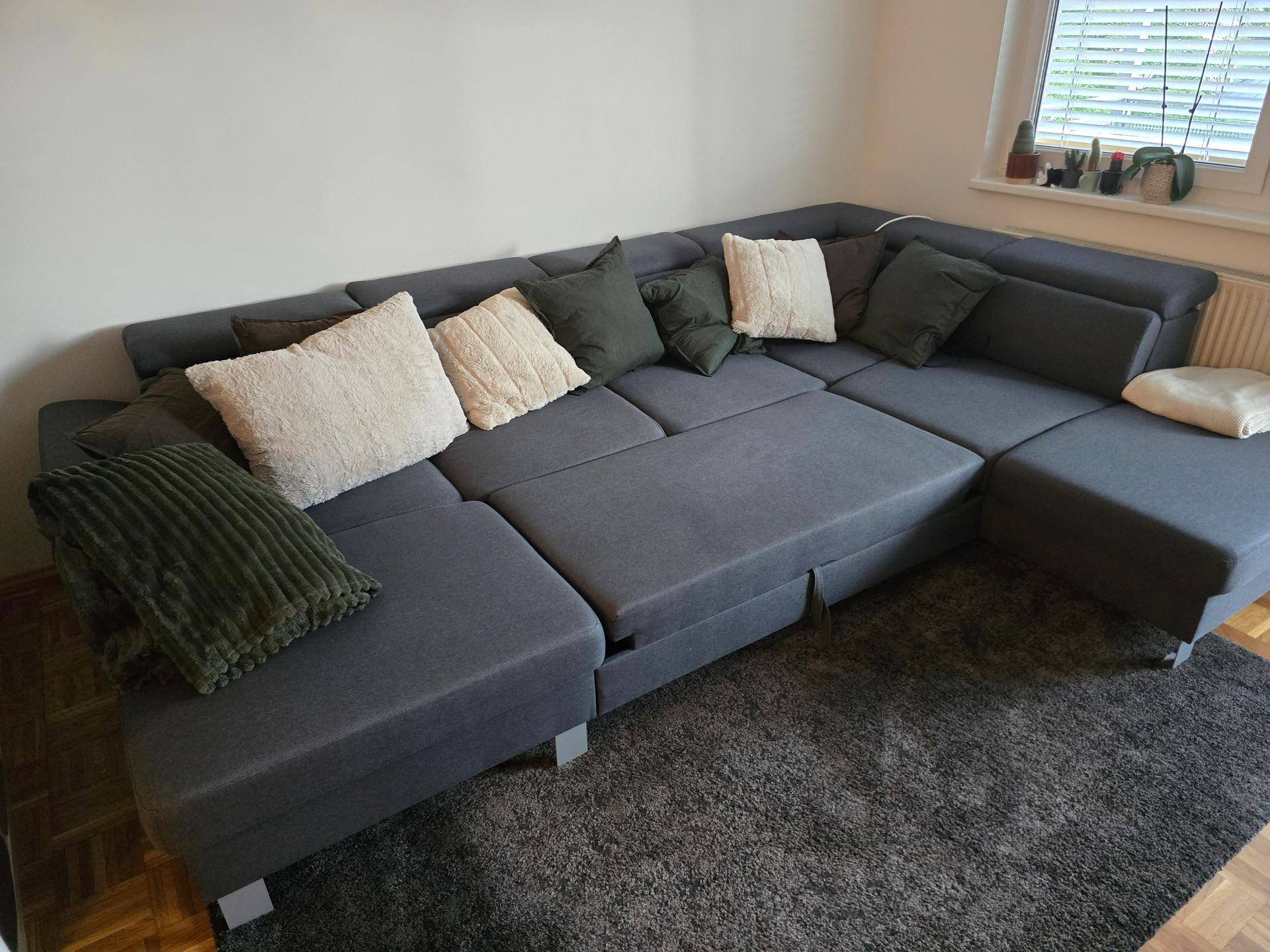 Gemütliches Wohnzimmer mit großem grauen Ecksofa, Teppich und Parkettboden.
