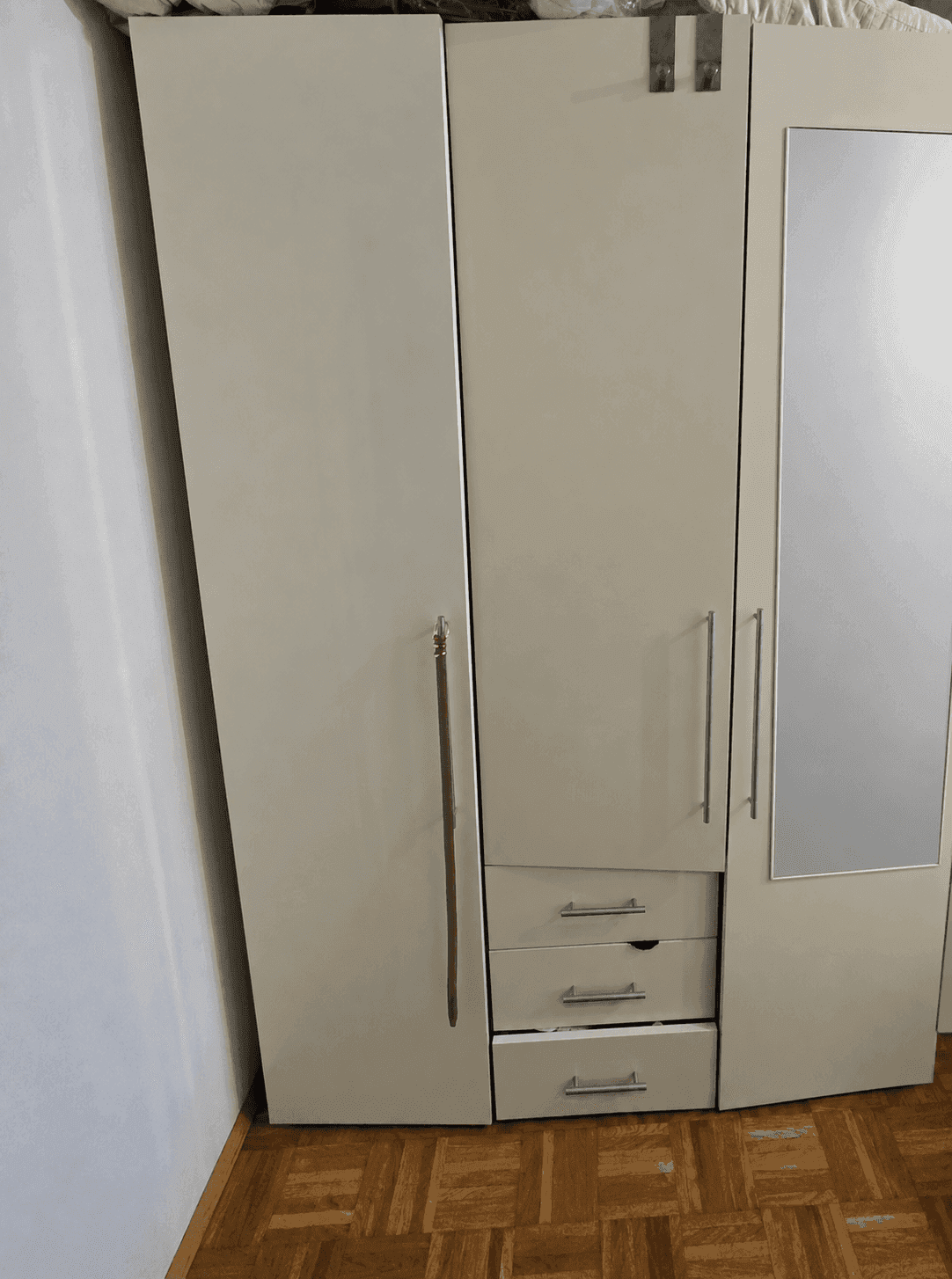 Heller Kleiderschrank mit Spiegeltür und Schubladen auf Parkettboden in einem Schlafzimmer.