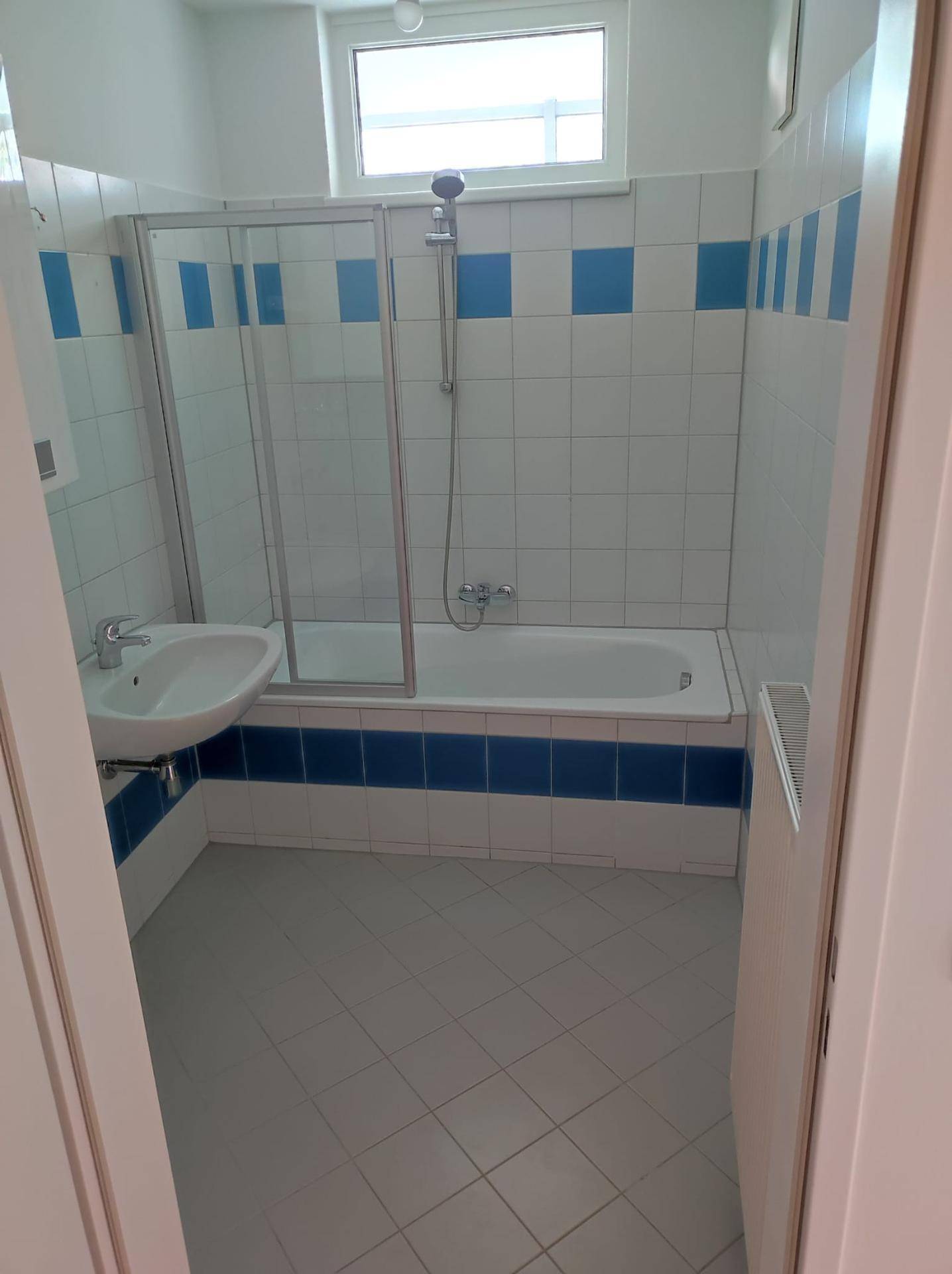 Badezimmer mit Badewanne, Duschabtrennung, Waschbecken, Fenster und blauen Akzentfliesen.
