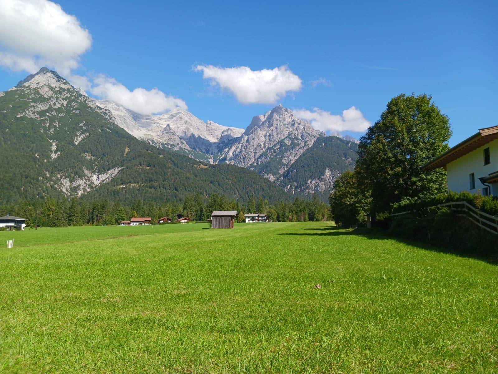 Malerische Landschaft mit grünen Wiesen, hohen Bergen und vereinzelten Häusern unter klarem Himmel.