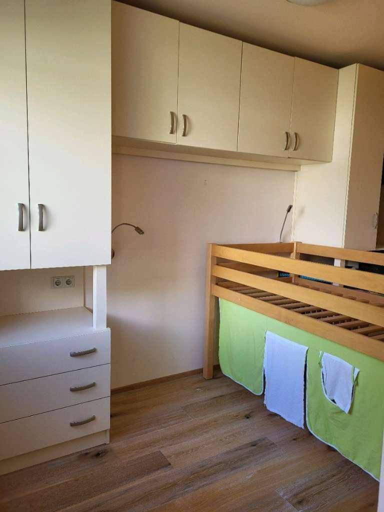 Kinderzimmer mit hellem Holzfußboden, Einbauschränken und einem Kinderbett.