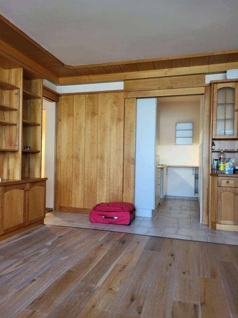 Wohnzimmer mit Holzwänden, Holzboden und Durchgang zu einem Küchenbereich.