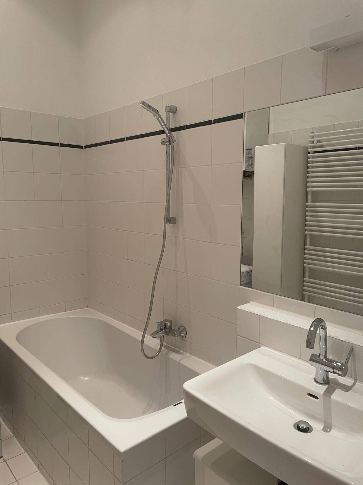 Modernes Badezimmer mit Badewanne, Einzelwaschbecken, Spiegel und beheiztem Handtuchhalter.
