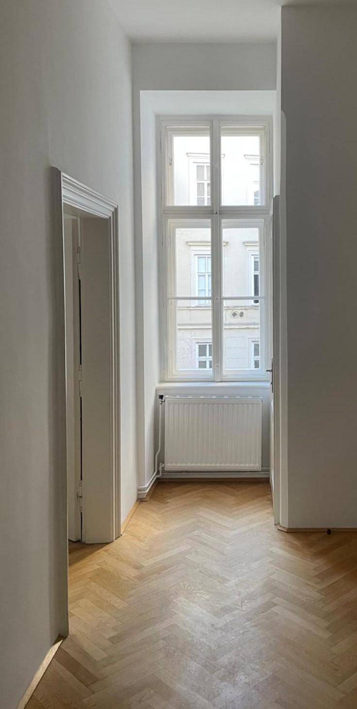 Schmaler Flur mit Fischgrätparkett und einem hohen Fenster, das einen Blick auf die Stadt bietet.