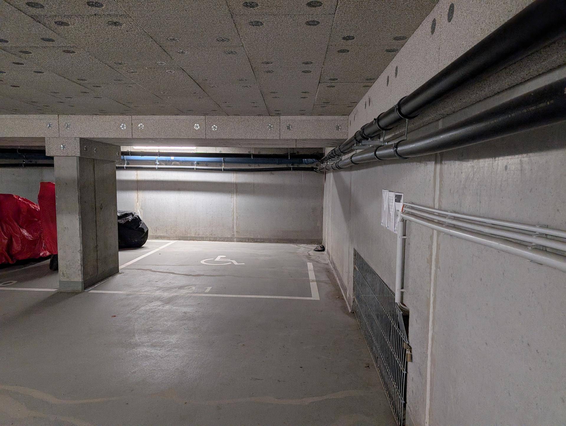 Heller Tiefgaragenstellplatz mit behindertengerechter Markierung und freiliegenden Rohren an der Decke.