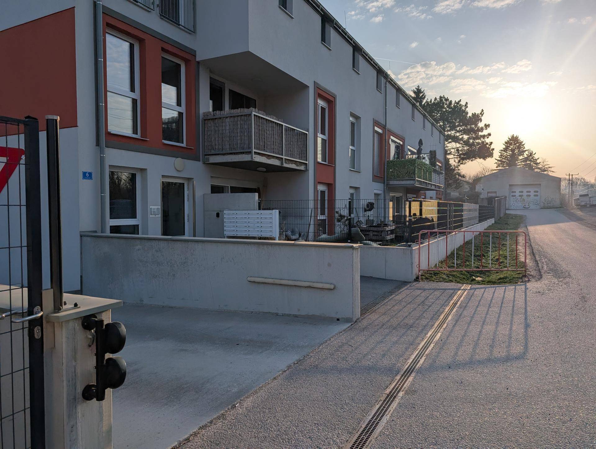 Moderne Wohnanlage mit Balkonen und Terrassen im Sonnenuntergang, umgeben von Grünflächen.