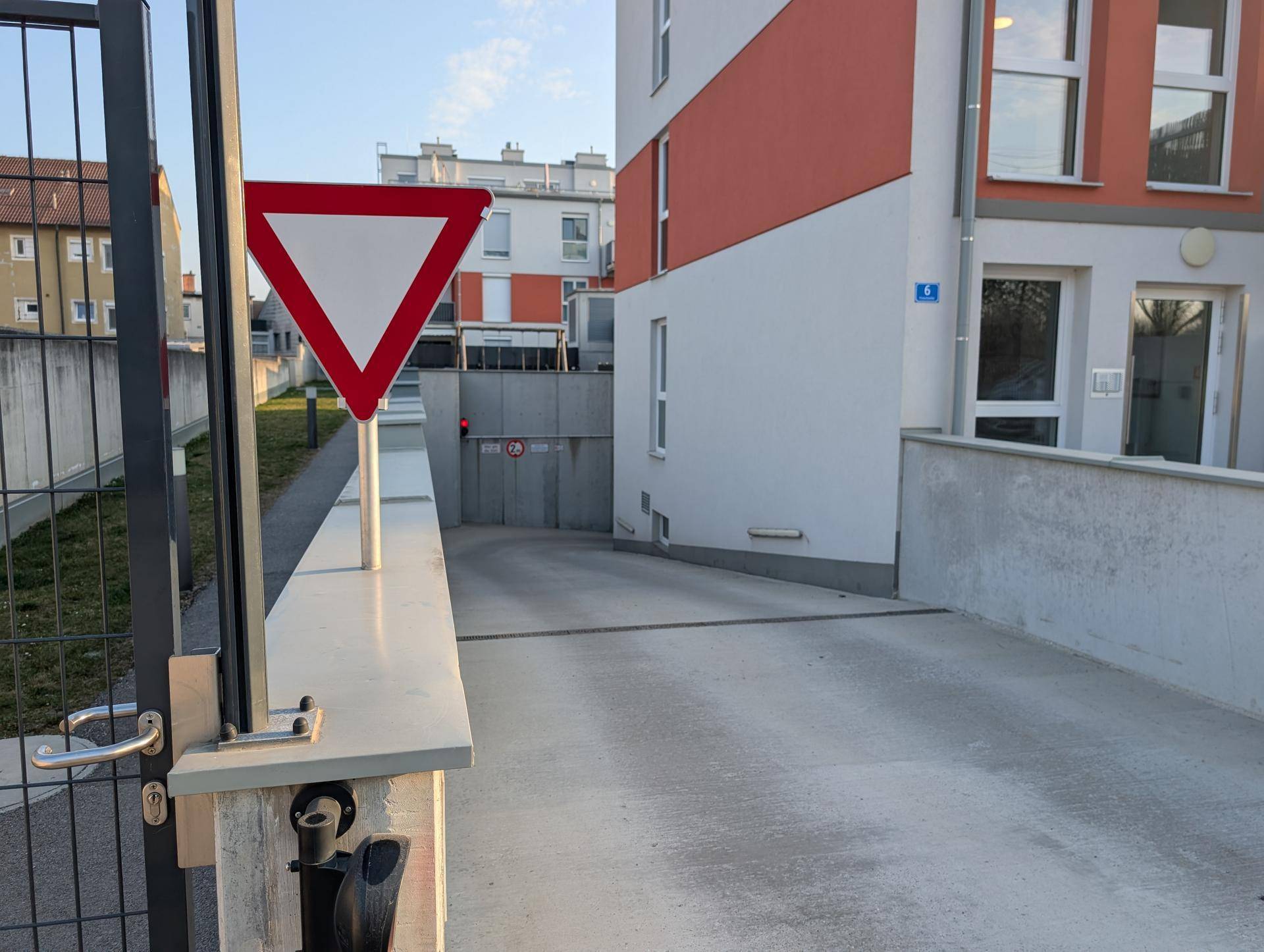 Einfahrt zur Tiefgarage einer modernen Wohnanlage mit Schranke und Verkehrsschild.