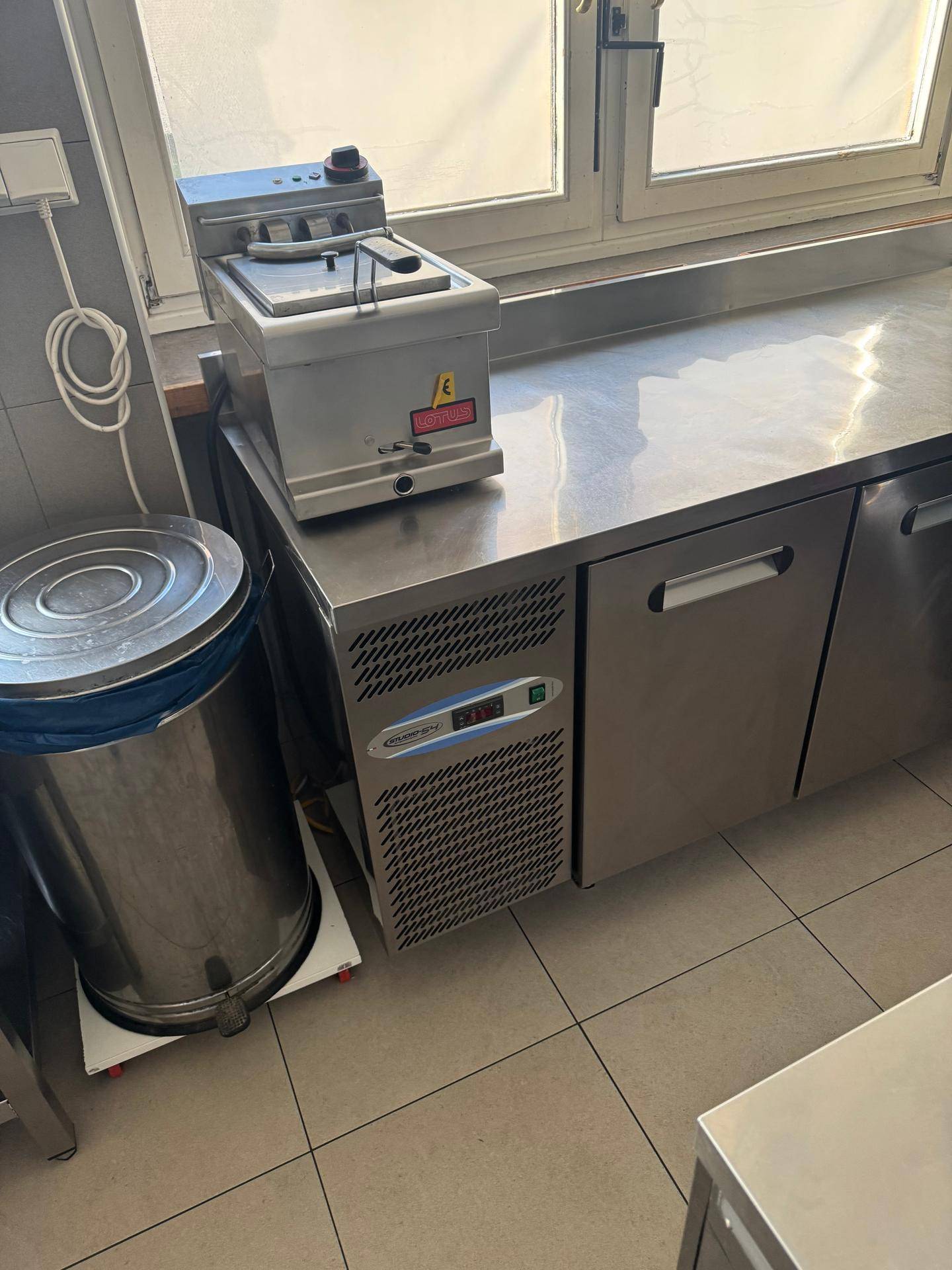 Edelstahlarbeitsfläche mit Fritteuse und Kühlschrank in einer professionellen Küche.