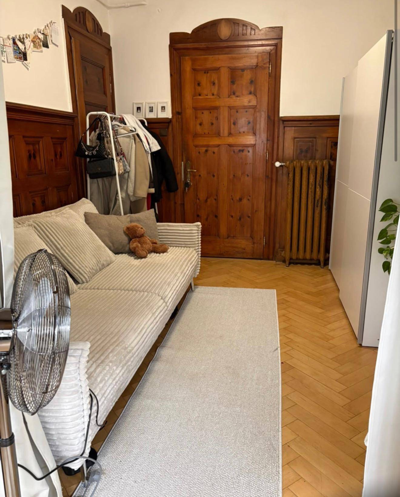 Wohnzimmer mit beigem Sofa, Holztür und einem klassischen Heizkörper.