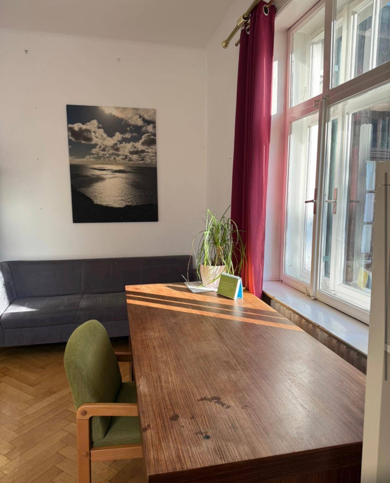 Heller Arbeitsbereich mit großem Holzschreibtisch, grünem Stuhl und einem Sofa.