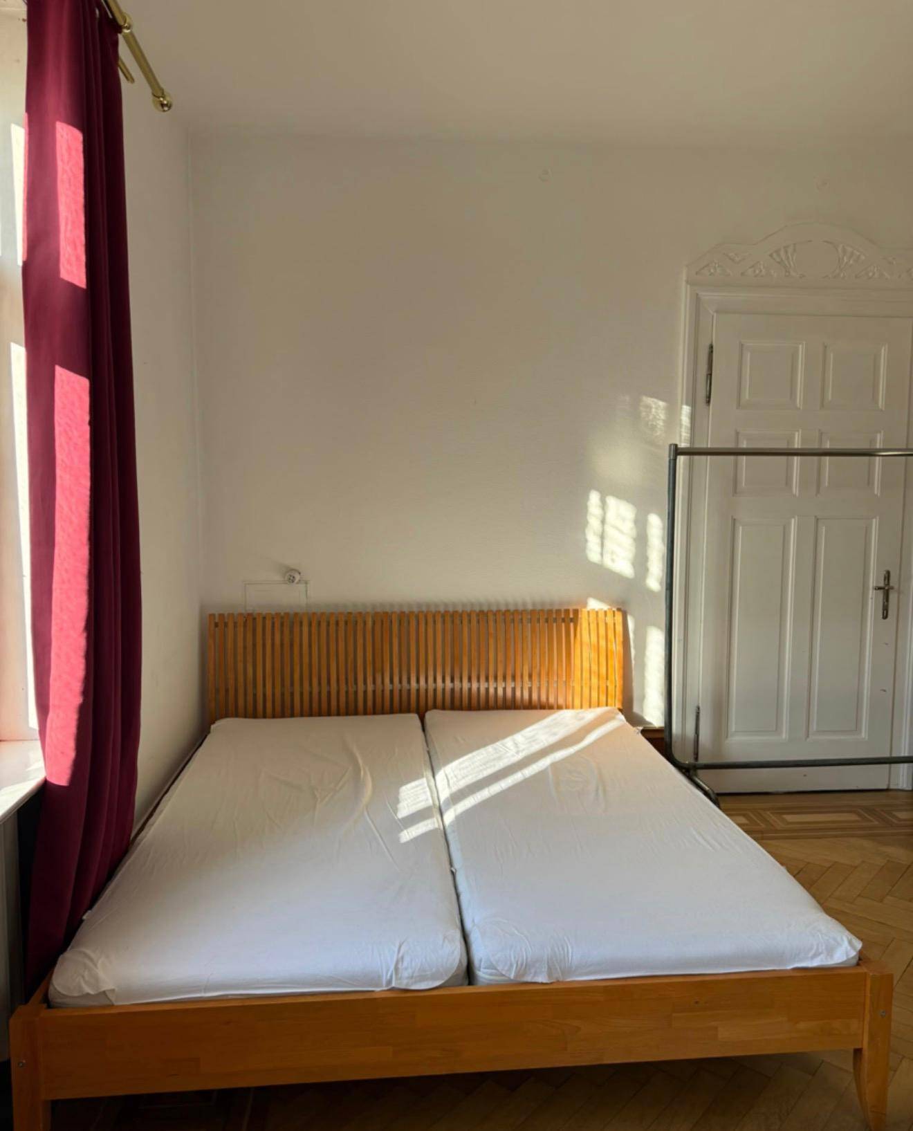 Helles Schlafzimmer mit Holzbett, weißen Wänden und roten Vorhängen am Fenster.