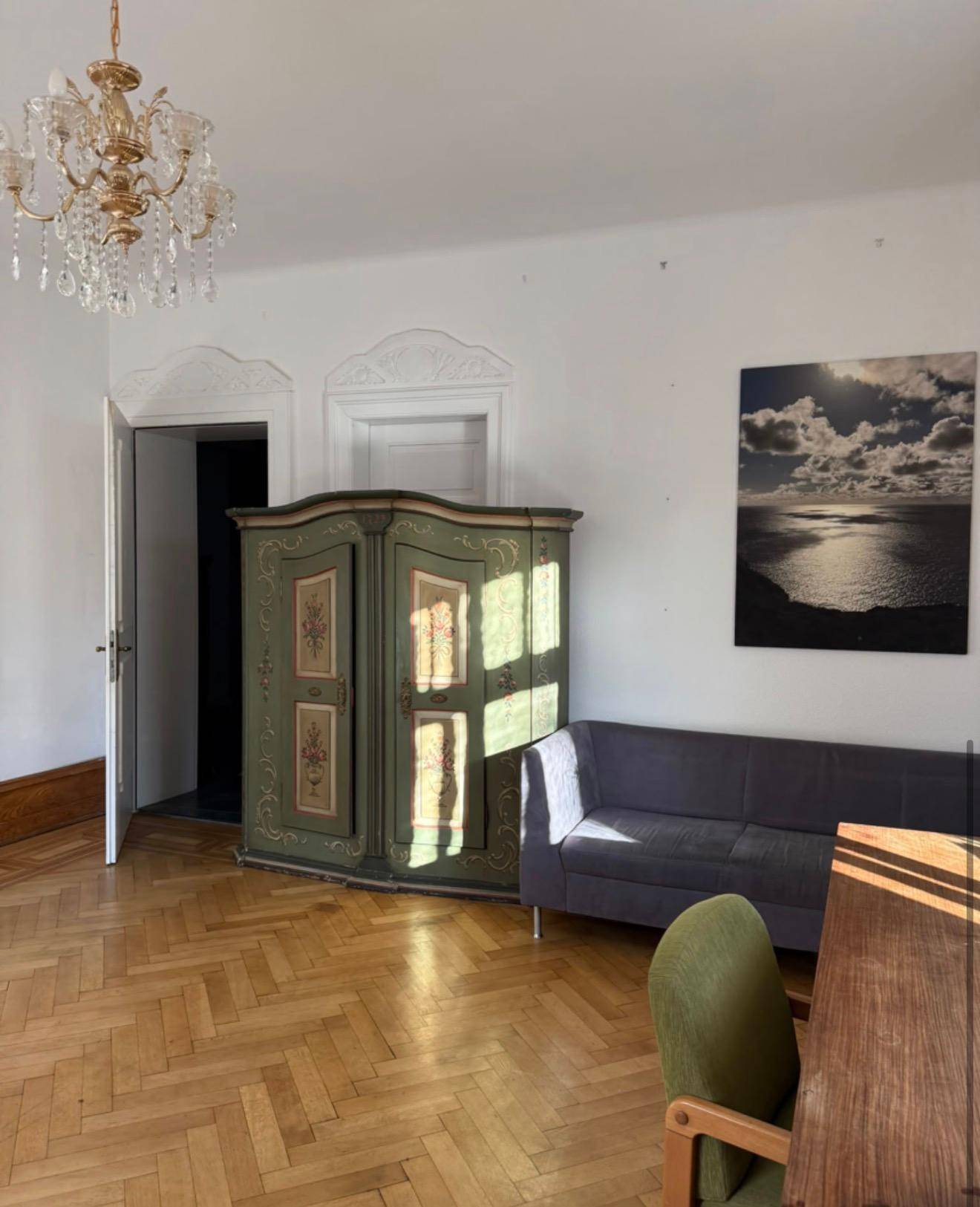 Wohnzimmer mit antikem grünem Schrank, Sofa und einem eleganten Kronleuchter.