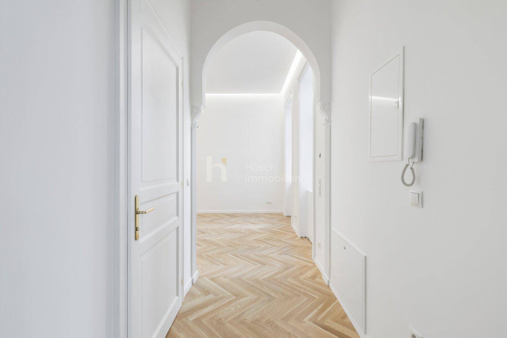 Heller Flur mit Fischgrätparkett und eleganten weißen Türen, der zu weiteren Räumen führt.